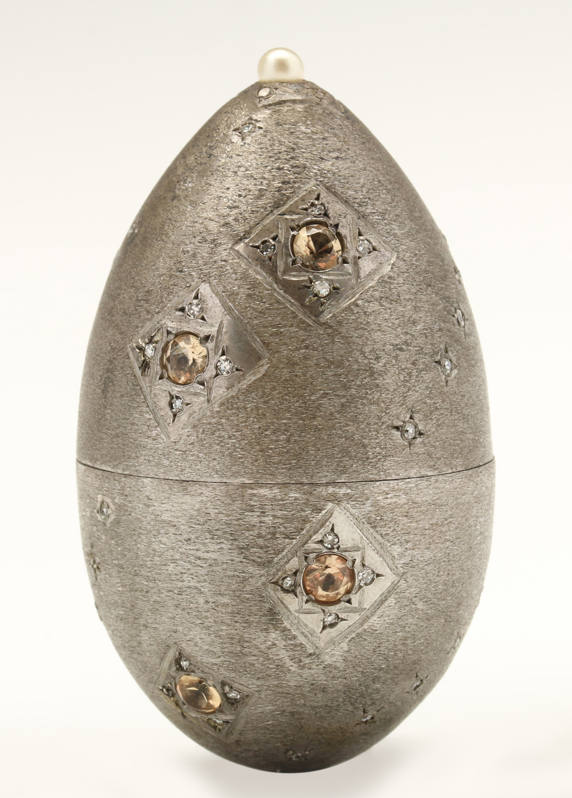 A BRUSHED METAL EGG SHAPE CONTAINER WITH GEMSTONES