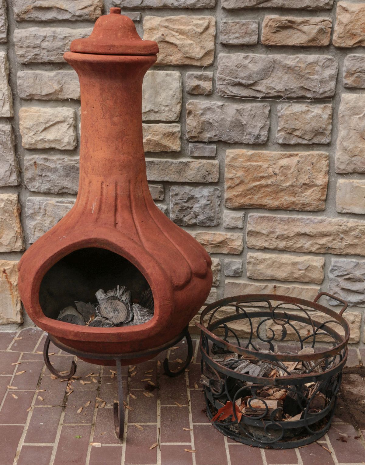 A RED CLAY CHIMINEA ON IRON STAND WITH WOOD HOLDER