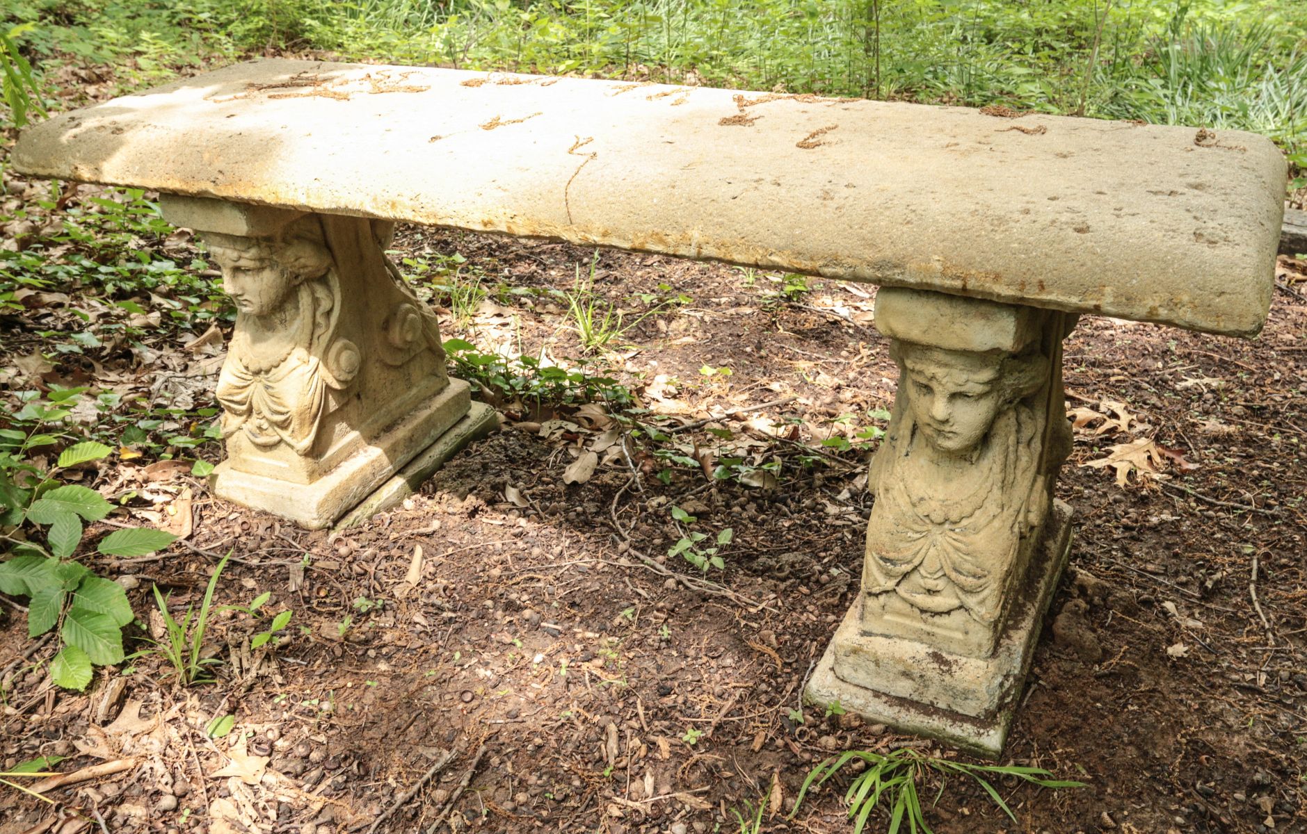 A CONCRETE GARDEN BENCH WITH CLASSICAL LADIES